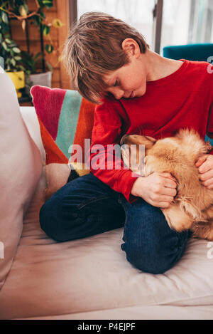 Ragazzo seduto sul divano abbracciando il suo golden retriever cane Foto Stock