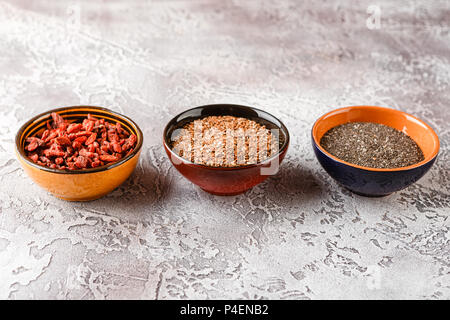 Super Foods - chia semi, semi di lino e bacche di goji in tre tazze di ceramica Foto Stock