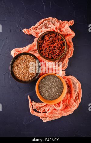 Super Foods - chia semi, semi di lino e bacche di goji in tre tazze di ceramica Foto Stock