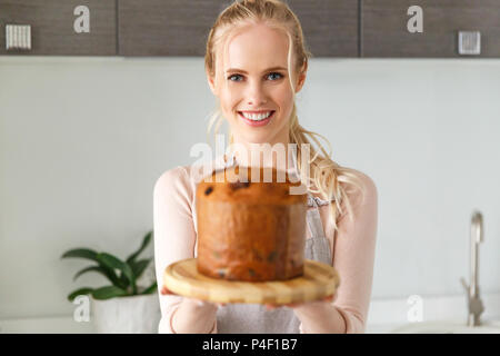 Giovane e bella donna bionda holding torta di Pasqua sulla tavola di legno e sorridente in telecamera Foto Stock