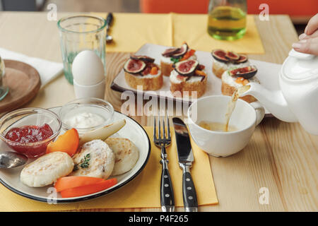 Ritagliato colpo di persona il versamento da tè teiera e gustosa colazione sana sul tavolo Foto Stock