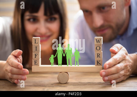 Coppia felice la protezione di equilibrio tra lavoro e vita familiare e carta ritagliata su altalena Foto Stock