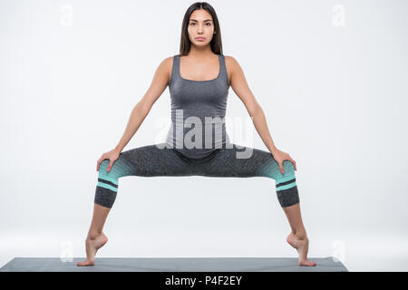 Asian donna incinta a praticare yoga in dea pongono, isolato su grigio Foto Stock