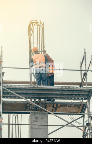 Lavoratori su impalcatura legato rebar e barre di acciaio, calcestruzzo pilastro in costruzione. In stile vintage. Foto Stock