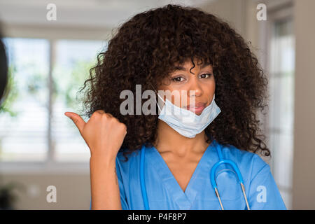 African American donna professionale medica rivolta con la mano e il dito verso l'alto con la faccia felice sorridente Foto Stock