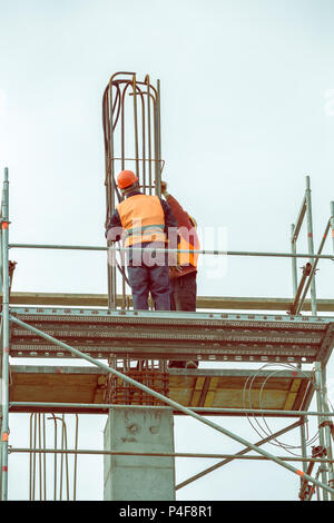 Lavoratori su impalcatura legato rebar e barre di acciaio, calcestruzzo pilastro in costruzione. In stile vintage. Foto Stock