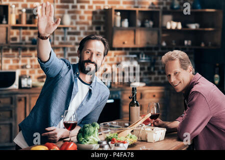 Allegro uomini di mezza età bere il vino e agitando la mano mentre si cucina insieme in cucina Foto Stock