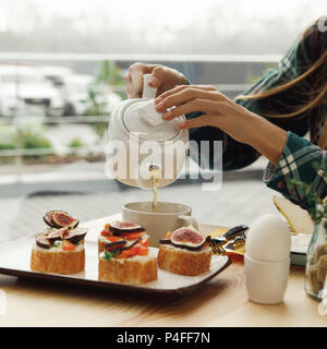 Ritagliato shot della ragazza versando da tè teiera pur avendo prima colazione Foto Stock