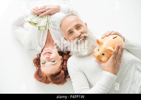 Sorridente Coppia matura con banconote di dollari e salvadanaio, isolato su bianco Foto Stock