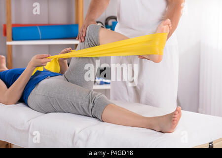 Fisioterapista dando trattamento gambe di donna con Giallo banda di esercizio Foto Stock