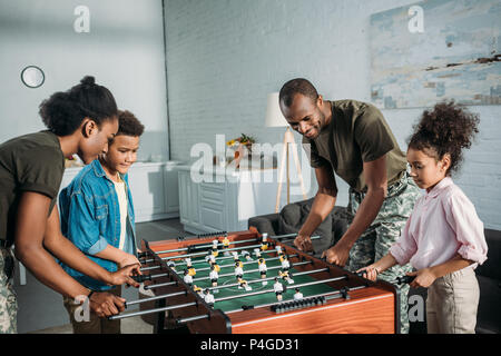 La famiglia felice del soldato genitori e afro-americano di ragazzi che giocano a calcio balilla Foto Stock