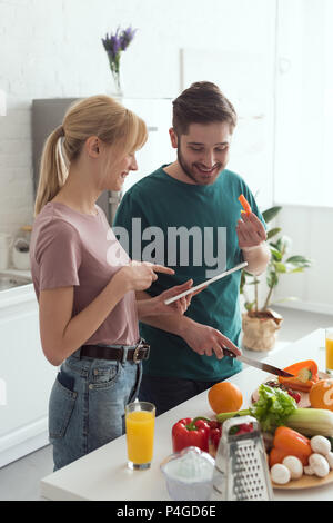 Paio di vegani utilizzando tablet con ricetta per preparare il cibo in cucina Foto Stock