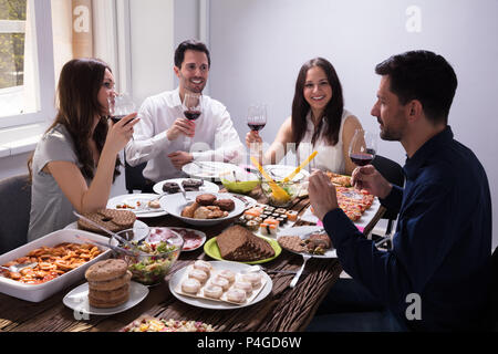 Sorridente giovani amici gustando cibo con un bicchiere di vino al ristorante Foto Stock