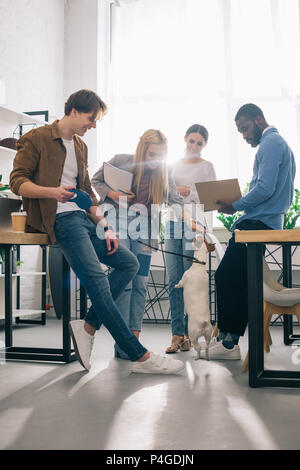 Multietnica di colleghi di lavoro con i libri di testo e jack russel terrier al guinzaglio in ufficio moderno Foto Stock