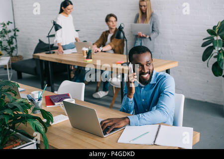 African American businessman parlando sullo smartphone e colleghi lavorando dietro Foto Stock