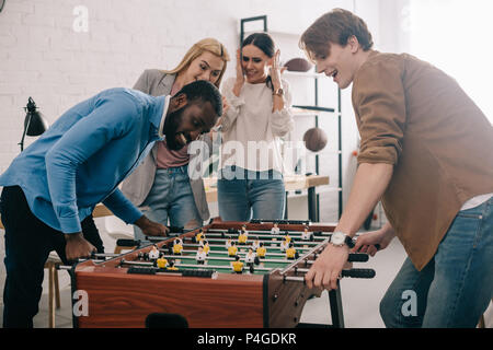 Vista laterale di felice imprenditori multiculturale la riproduzione di calcio da tavolo di fronte ai colleghi di sesso femminile Foto Stock