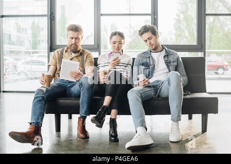 Professional business i colleghi uomini e donna cercando in schermate dei dispositivi digitali in un ufficio moderno Foto Stock