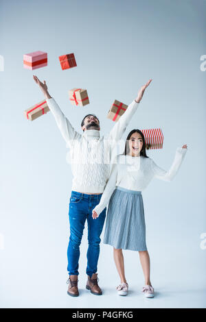 Coppia multiculturale cattura la caduta di avvolgere i regali di Natale isolato su grigio Foto Stock