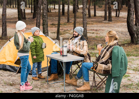 Felice famiglia giovane sul campeggio nella foresta di bere il tè caldo Foto Stock