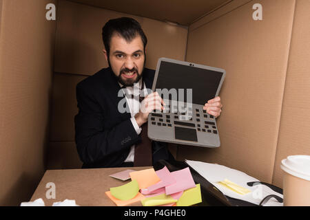 Angry businessman holding laptop di cartone nella casella Foto Stock