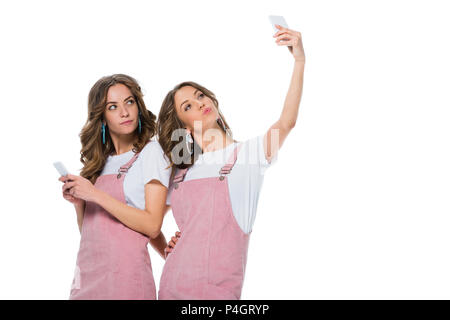 Attraente giovane gemelli tenendo selfie con lo smartphone isolato su bianco Foto Stock