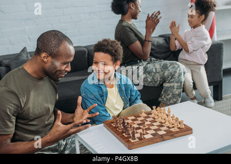 Uomo in Abbigliamento camouflage insegnare a suo figlio di giocare a scacchi mentre madre e figlia insieme giocando Foto Stock