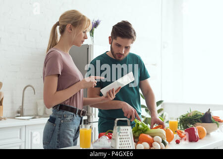 Ragazza puntando su tablet con ricetta durante la cottura in cucina, concetto vegan Foto Stock