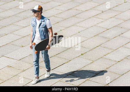 Angolo di alta vista del bel giovane uomo a camminare con lo skateboard in mano Foto Stock