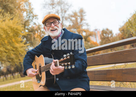 Felice barbuto elegante uomo senior giocando sulla chitarra acustica in autunno park Foto Stock