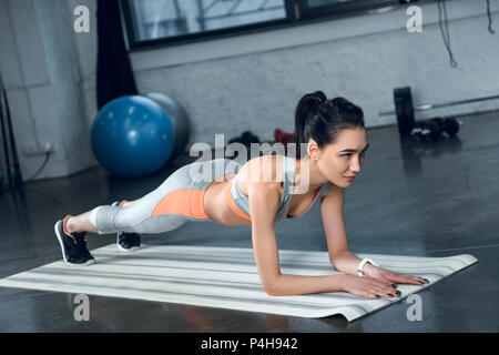 Montare la giovane donna facendo plank sul materassino yoga in palestra Foto Stock