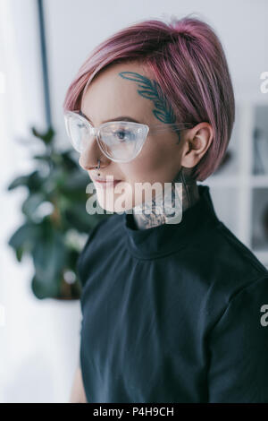 Sorridente giovane imprenditrice con tatuaggi indossando occhiali e guardando lontano Foto Stock