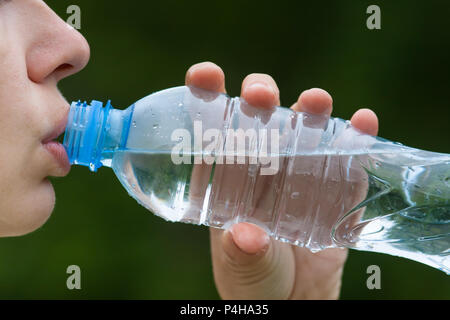Donna di bere acqua da una bottiglia su sfondo natura Foto Stock