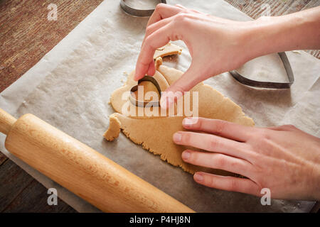 Donna con le sue mani intaglia i biscotti allo zenzero in forma di cuori con un metallo forma su di un tavolo di legno Foto Stock