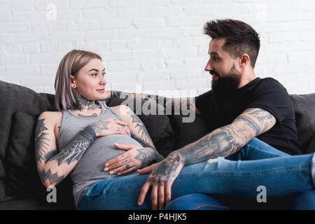 Tatuato incinta ragazza sdraiato con il fidanzato sul divano di casa Foto Stock