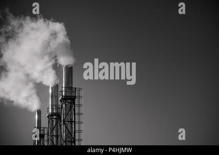 Tre tubi di fumo di un impianto contro il cielo. Il concetto di inquinamento ambientale. Foto in bianco e nero con spazio di copia Foto Stock