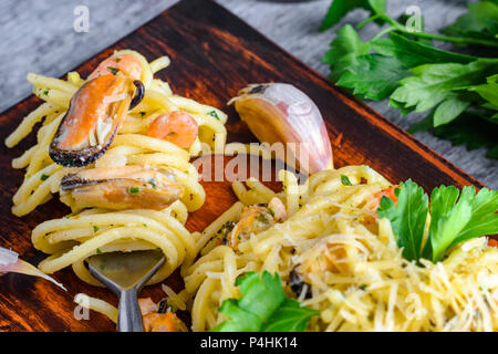 Pasta con frutti di mare cozze e gamberi in una salsa cremosa e un mazzetto di prezzemolo su una piastra. Foto Stock