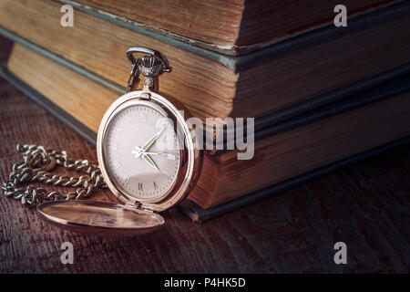 Comporre Vintage orologio da tasca su una catena e vecchi libri su uno sfondo di legno. Immagine oscurata in chiave di basso Foto Stock