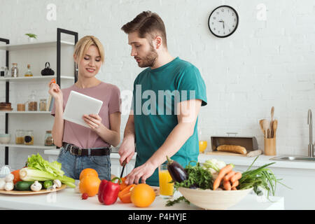 Paio di vegani utilizzando tablet con ricetta per la cottura in cucina Foto Stock