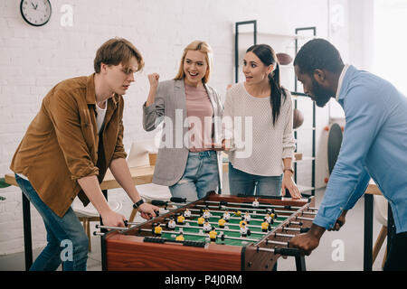 Vista laterale di uomini di affari multiculturali riproduzione di calcio da tavolo di fronte ai colleghi di sesso femminile Foto Stock