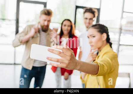 Vista ravvicinata di smartphone in mano sulla donna prendendo selfie con il suo team di business in un ufficio moderno Foto Stock