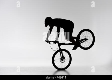 Silhouette di un ciclista prova eseguendo cavalletto anteriore su bianco Foto Stock