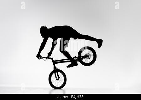 Silhouette di trial biker esecuzione di equilibratura delle ruote anteriori stunt in bicicletta su bianco Foto Stock