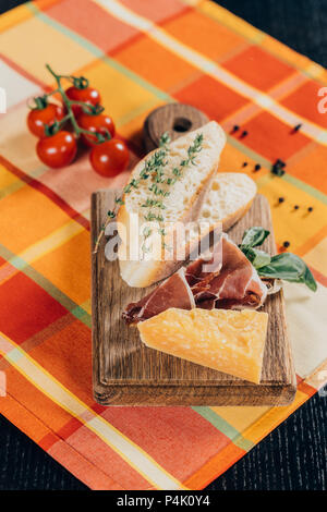 Vista ravvicinata della baguette affettata, carne e formaggio parmigiano sul tagliere di legno e freschi pomodori ciliegia sulla tavola Foto Stock