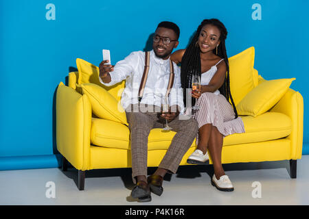 Sorridente giovane americano africano giovane azienda di bicchieri di vino e tenendo selfie con lo smartphone sul lettino Foto Stock