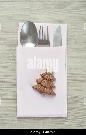 Una semplice impostazione del luogo per il Natale costituito da una forcella, coltello, un tovagliolo bianco e una forma di cioccolato albero di natale Foto Stock