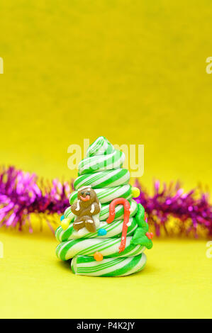 Un candy cane albero di Natale visualizzati con tinsel viola su sfondo giallo Foto Stock