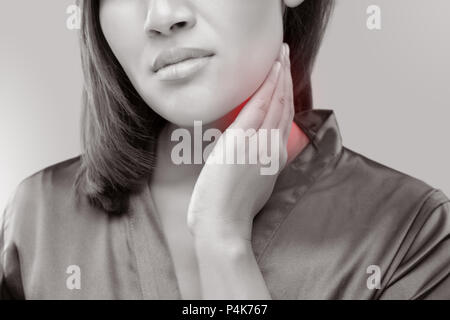 Una donna con il mal di gola mentre tiene il suo collo, su uno sfondo grigio, linfoadenopatia, le persone con problemi di salute concetto. Foto Stock