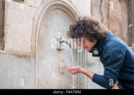 Piuttosto giovane con capelli ricci di bere acqua da una fontana Foto Stock