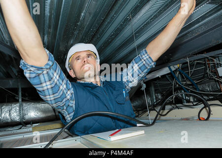 Uomo di riparazione di un cablaggio elettrico sul soffitto Foto Stock