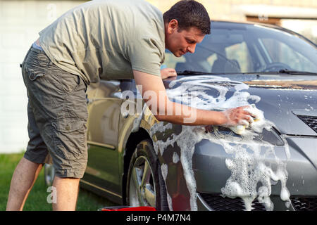 Uomo bello il lavaggio auto con una spugna e schiuma nel cortile di